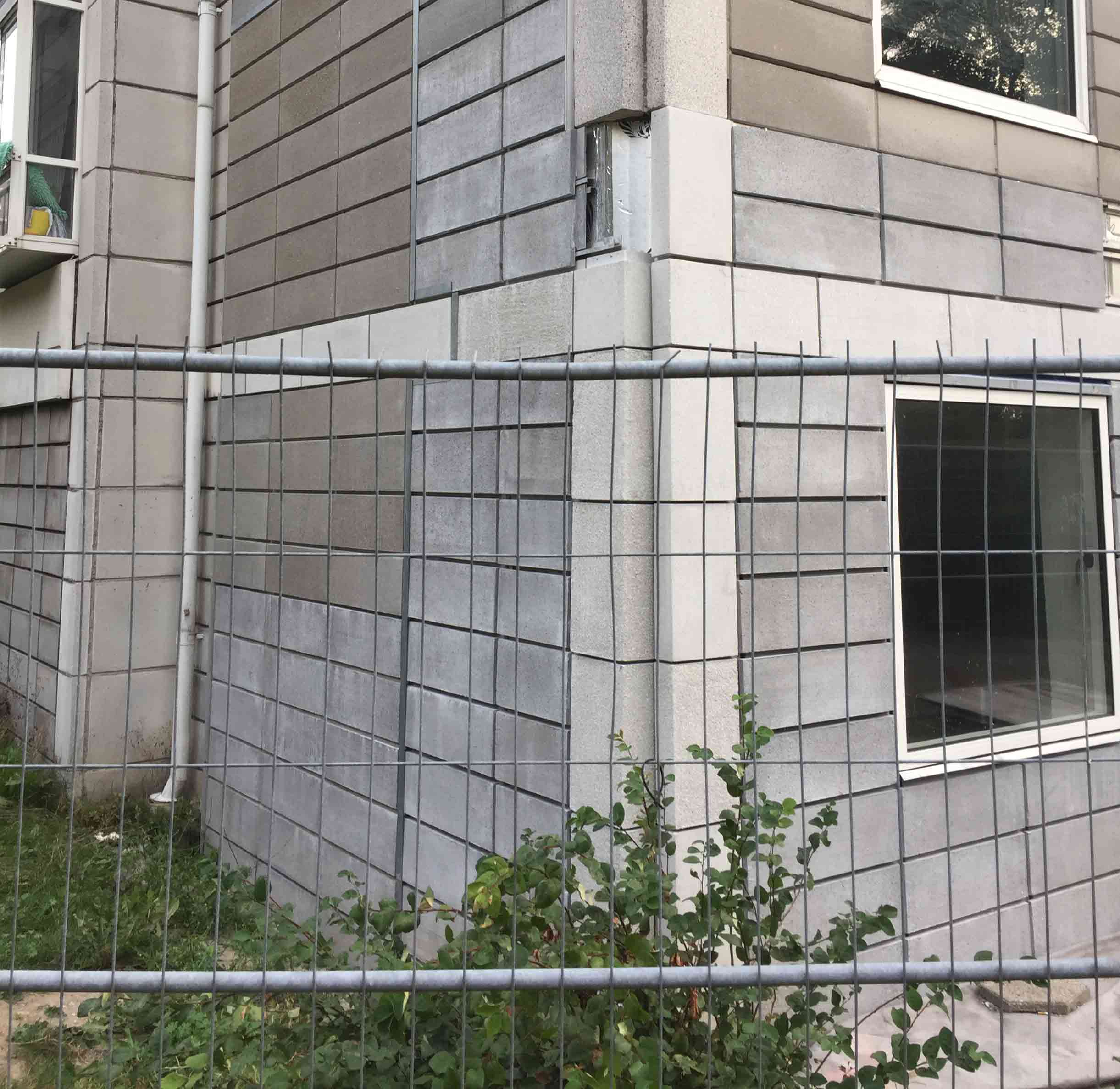 Et midlertidigt hegn omgiver flere af Bellahøjhusene for at beskytte beboerne mod nedfaldne facadefliser. Det er samtidig et eksempel på de dilemmaer, der kan opstå, når man skal renovere bevaringsværdigt alment boligbyggeri.